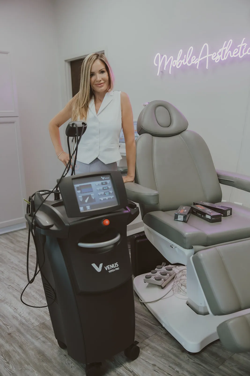 Amy Palacios, FNP, beside the Venus Versa Pro platform in her Harrisburg medspa, beneath the Mobile Aesthetics neon.